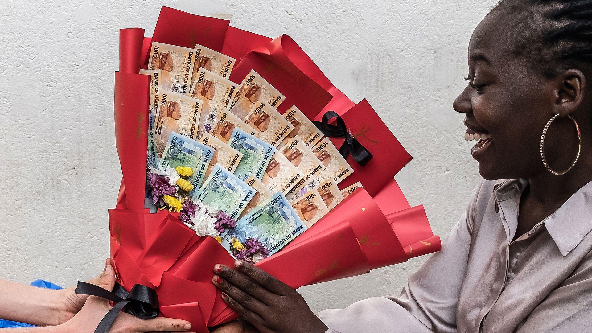 Një grua buzëqesh ndërsa merr një buqetë të bërë me kartëmonedha dhe lule nga i dashuri i saj si surprizë përpara Ditës së Shën Valentinit, gjatë një takimi në Kampala më 7 shkurt 2026.  