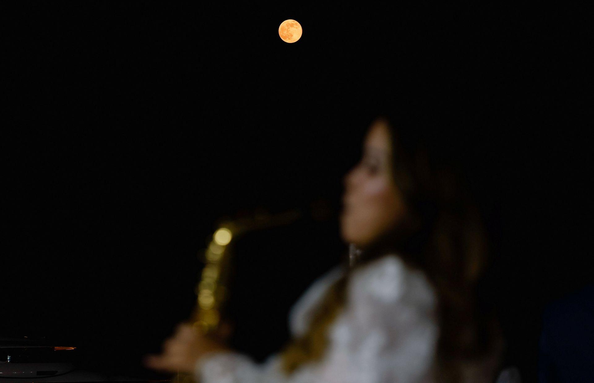 Muzikantja femër mund të shihet në plan të parë, por jashtë fokusit, ndërsa Hëna shkëlqen shumë portokalli kundrejt një qielli nate pa yje në Doha të mërkurën.