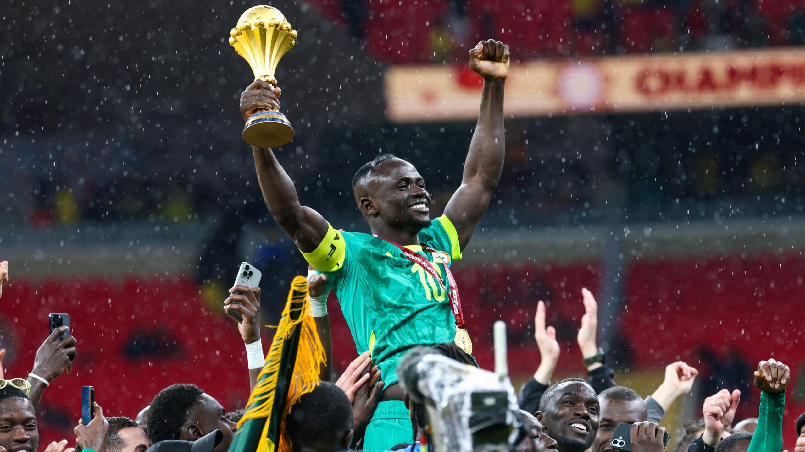 Sadio Mane ngrihet lart nga shokët e ekipit të Senegalit ndërsa mban lart trofeun e Kupës së Kombeve të Afrikës në dorën e djathtë.