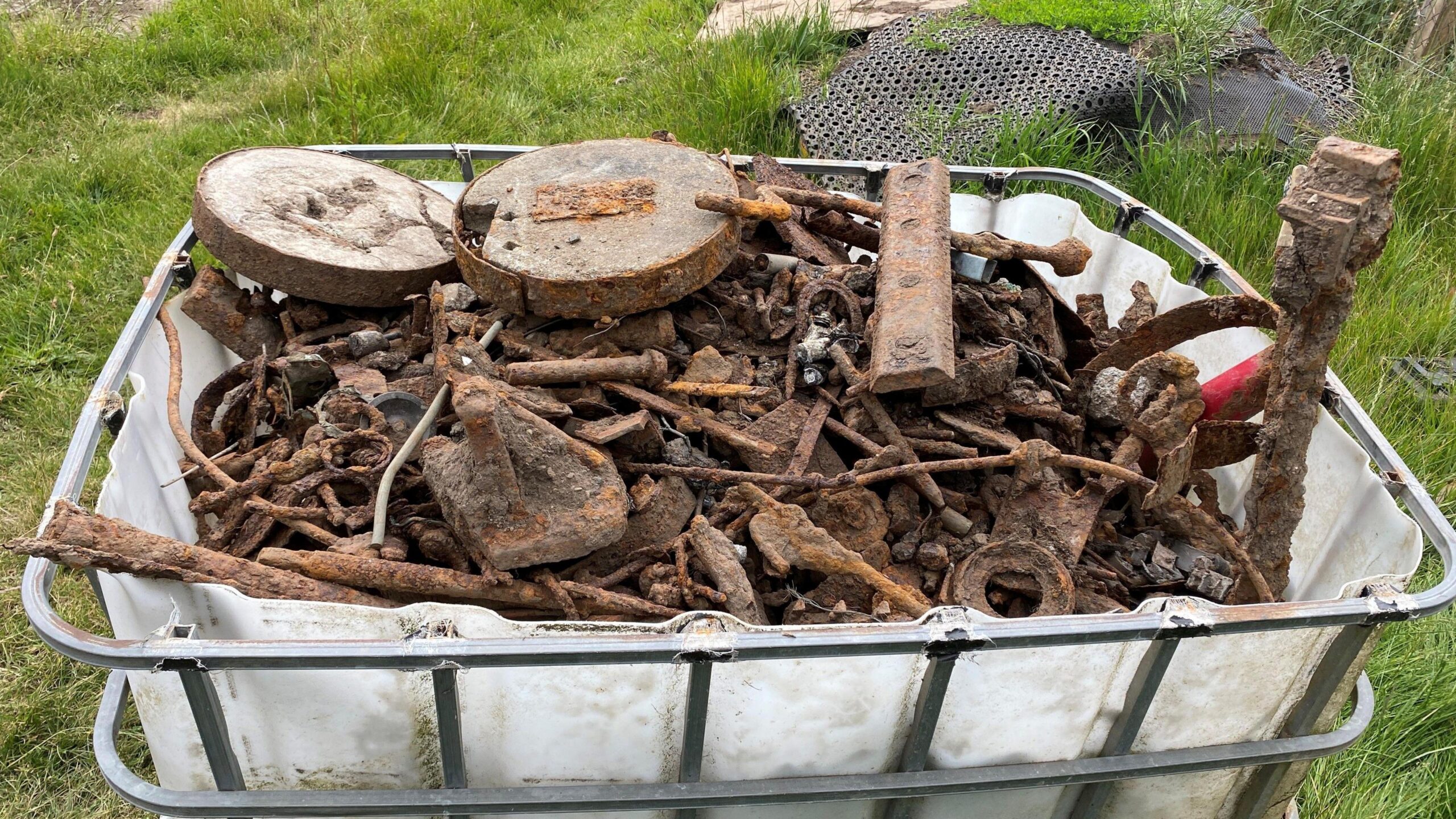 Një enë plastike e bardhë me një unazë metalike mban një sasi të madhe mbeturinash metalike, duke përfshirë tuba, këpucë kali dhe unaza metalike.