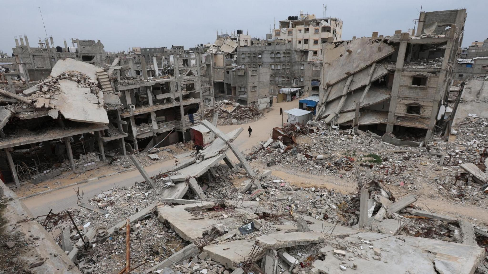 Palestinezët ecin pranë ndërtesave të shkatërruara në Khan Younis, në jug të Gazës (22 janar 2026)