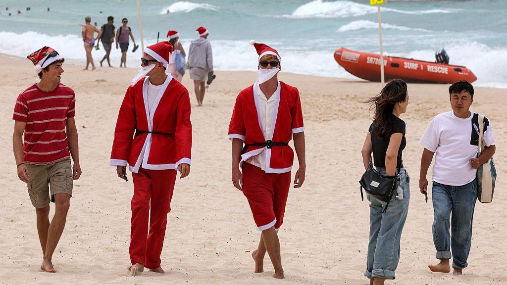 Njerëz të veshur me kostume të Babagjyshit ecin përgjatë rërës së plazhit Bondi në Sydney, Australi më 25 dhjetor 2025.