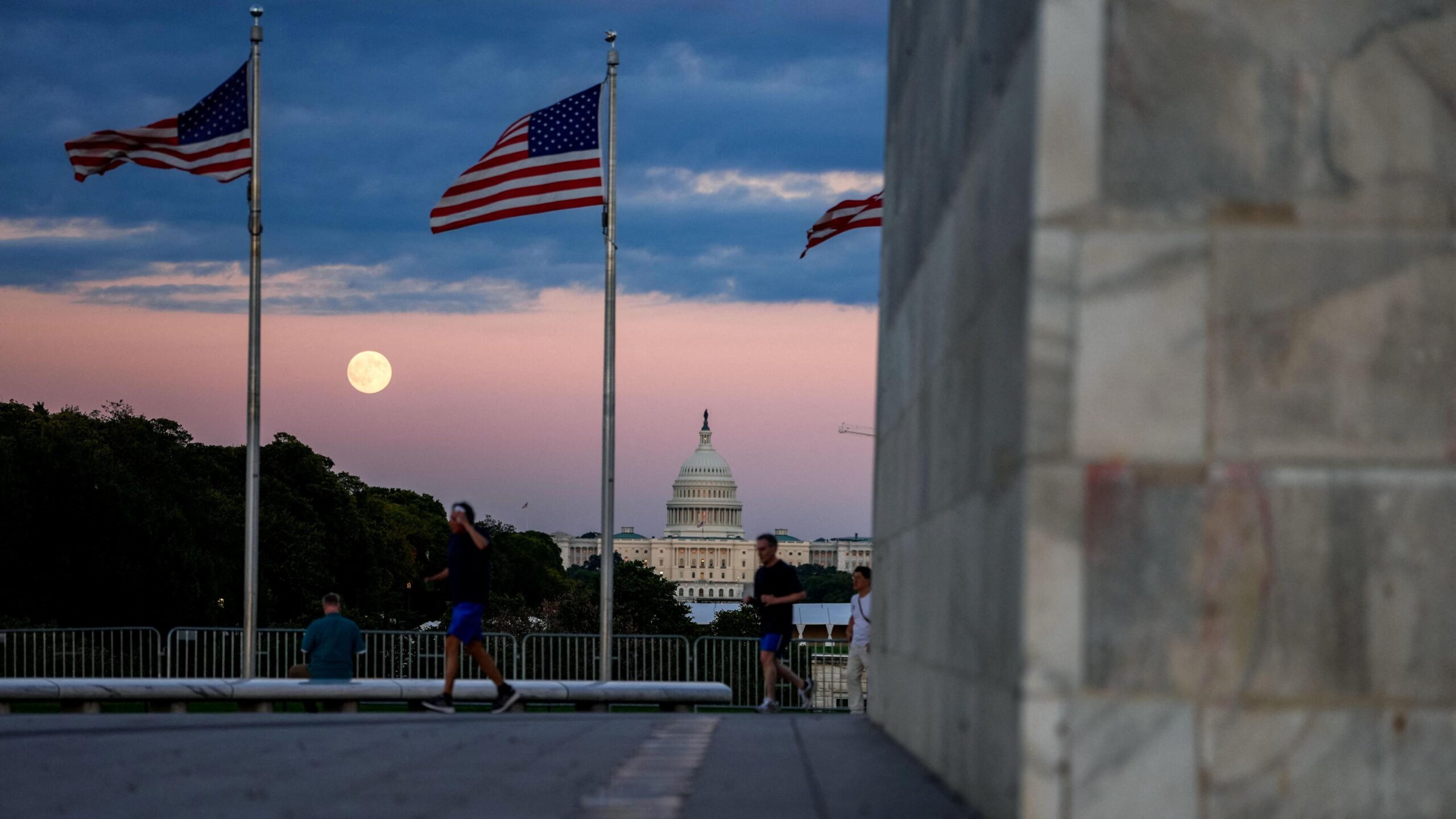 Superhëna shfaqet midis dy flamujve amerikanë dhe mbi ndërtesën e Kapitolit të SHBA-së në një pamje nga larg të National Mall.