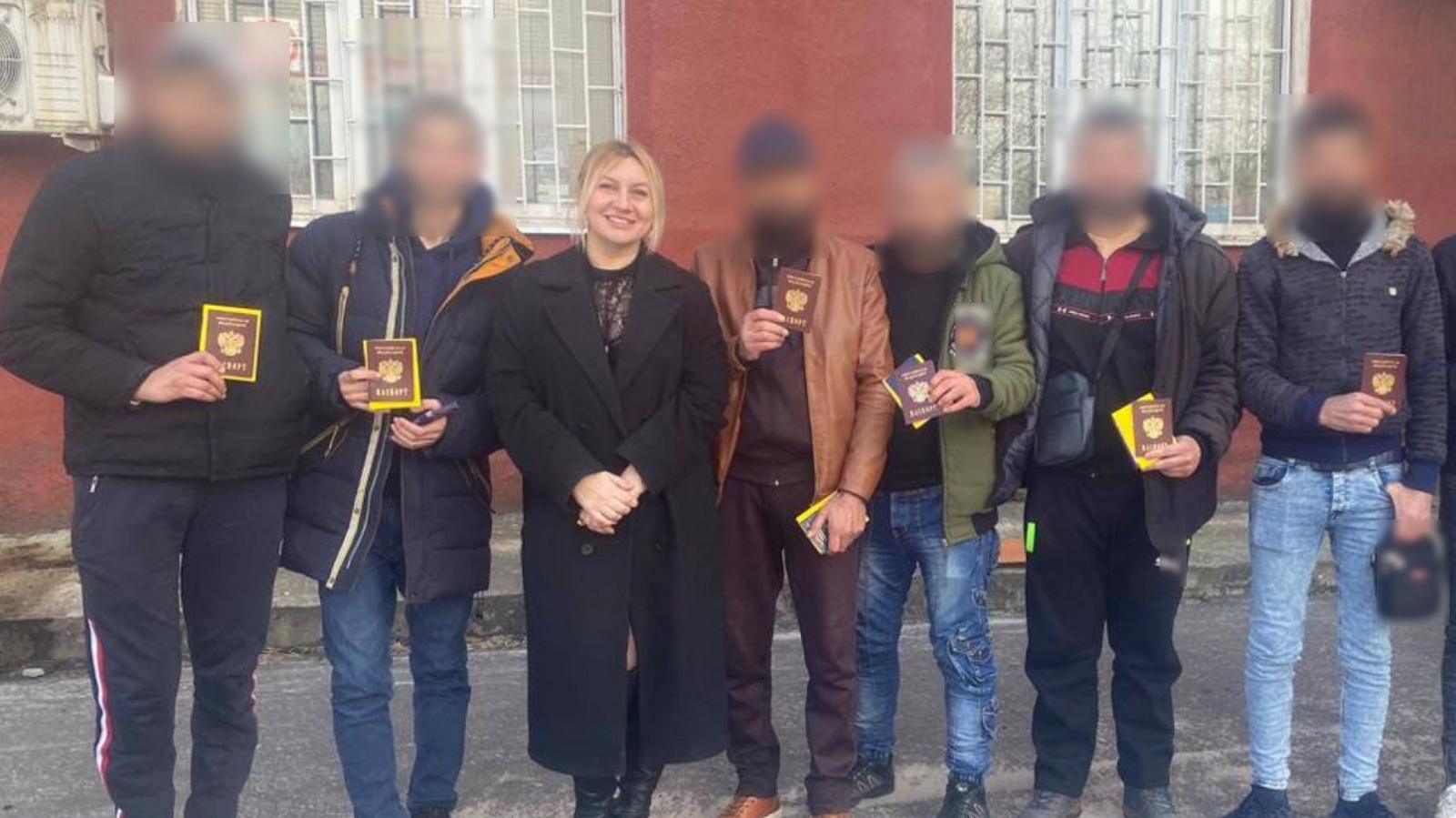 Polina Azarnykh qëndron duke buzëqeshur, e veshur me një pallto të gjatë të zezë dhe çizme elegante të zeza, në një rresht burrash të veshur me xhinse, këpucë të përditshme dhe xhaketa. Fytyrat e tyre janë errësuar për të fshehur identitetin e tyre. Ata mbajnë lart dokumente udhëtimi ruse.