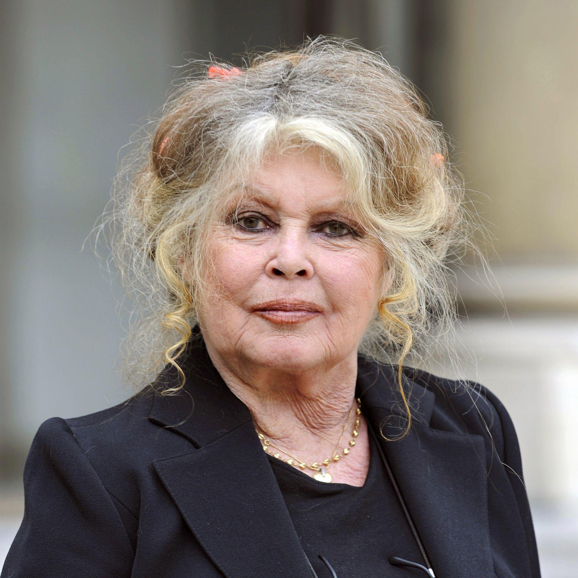 Brigitte Bardot e fotografuar jashtë Pallatit Elysee, e veshur me një kostum të zi dhe me masën e flokëve të saj bjonde paksa të thinjura.