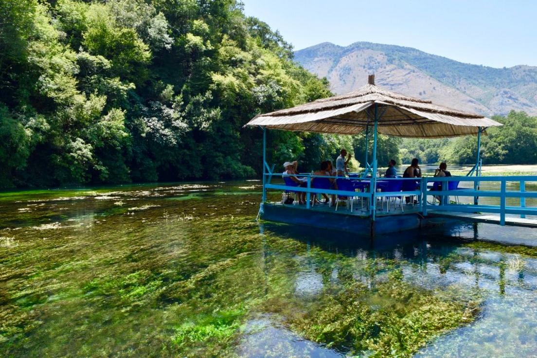 Një verandë në një lumë në Shqipëri. Uji është kristal i pastër dhe mund të shihni bimët e gjelbra në shtratin e lumit. Është vapë dhe me diell.