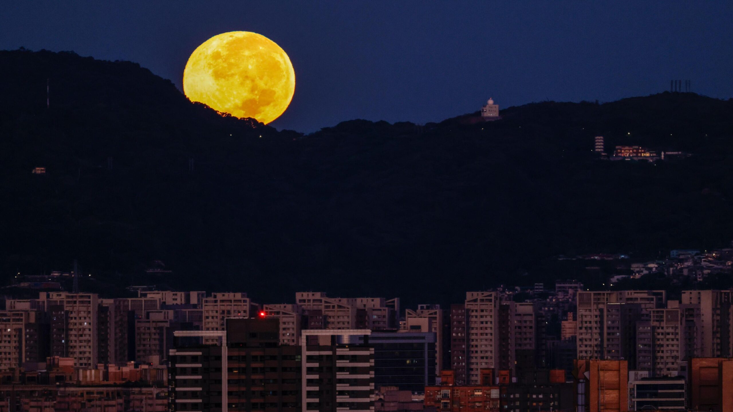 Një superhënë e ndritshme me ngjyrë të verdhë shfaqet pas një peizazhi malor që kufizohet me qytetin e Taipeit.