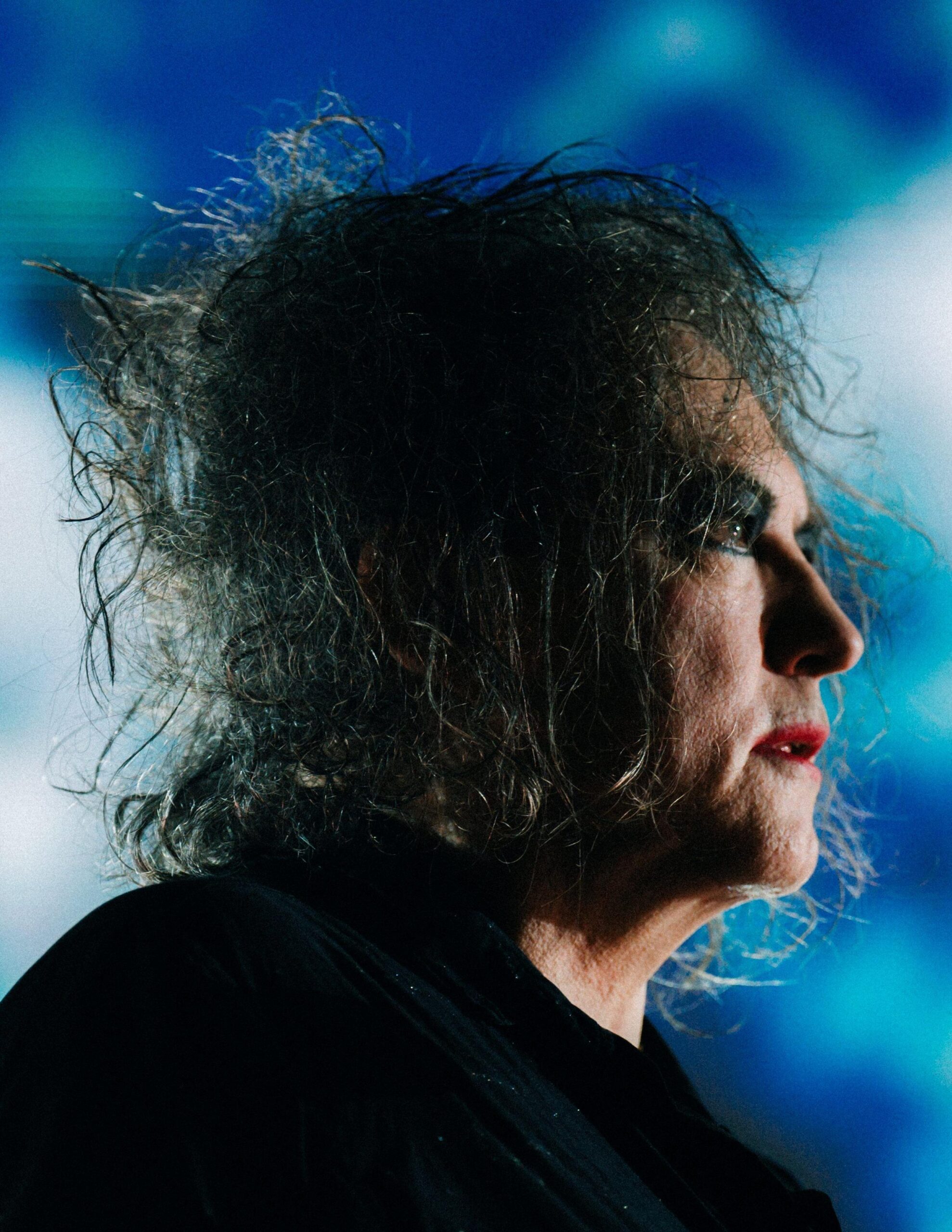 Foto profili e Robert Smith të The Cure në një sfond blu. Smith ka vënë grim të zi për sytë dhe buzëkuq të kuq.