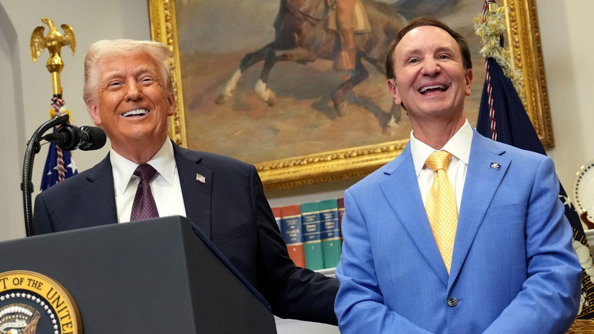 Presidenti i SHBA-së, Donald Trump, me kostum të zi dhe guvernatori i Luizianës, Jeff Landry, me kostum blu, buzëqeshin ndërsa qëndrojnë në një podium.