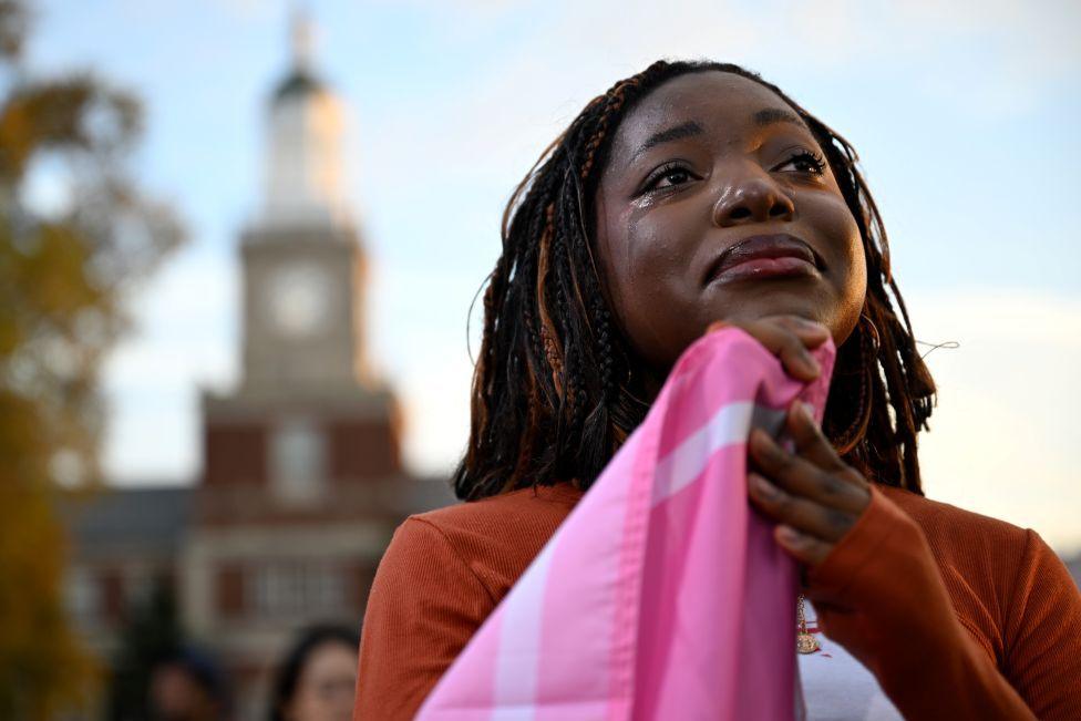 Një grua afrikano-amerikane mban një flamur dhe duket e përlotur ndërsa dëgjon kandidaten demokrate për presidente Kamala Harris të pranojë fitoren gjatë një fjalimi në Universitetin Howard.