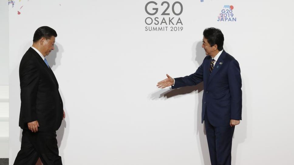 Presidenti kinez Xi Jinping shikon poshtë ndërsa ecën drejt kryeministrit japonez Shinzo Abe, i cili i zgjat dorën me një buzëqeshje.