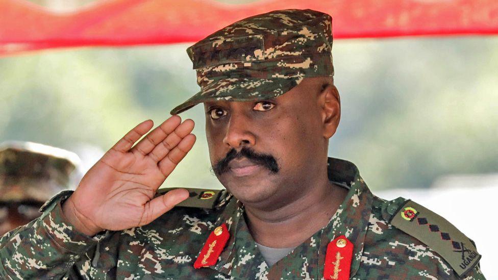 Gjenerali Muhoozi Kainerugaba përshëndet në një garë stërvitjeje ushtarake. Ai mban veshur uniforma ushtarake - epauletat e tij tregojnë se është një gjeneral me katër yje.