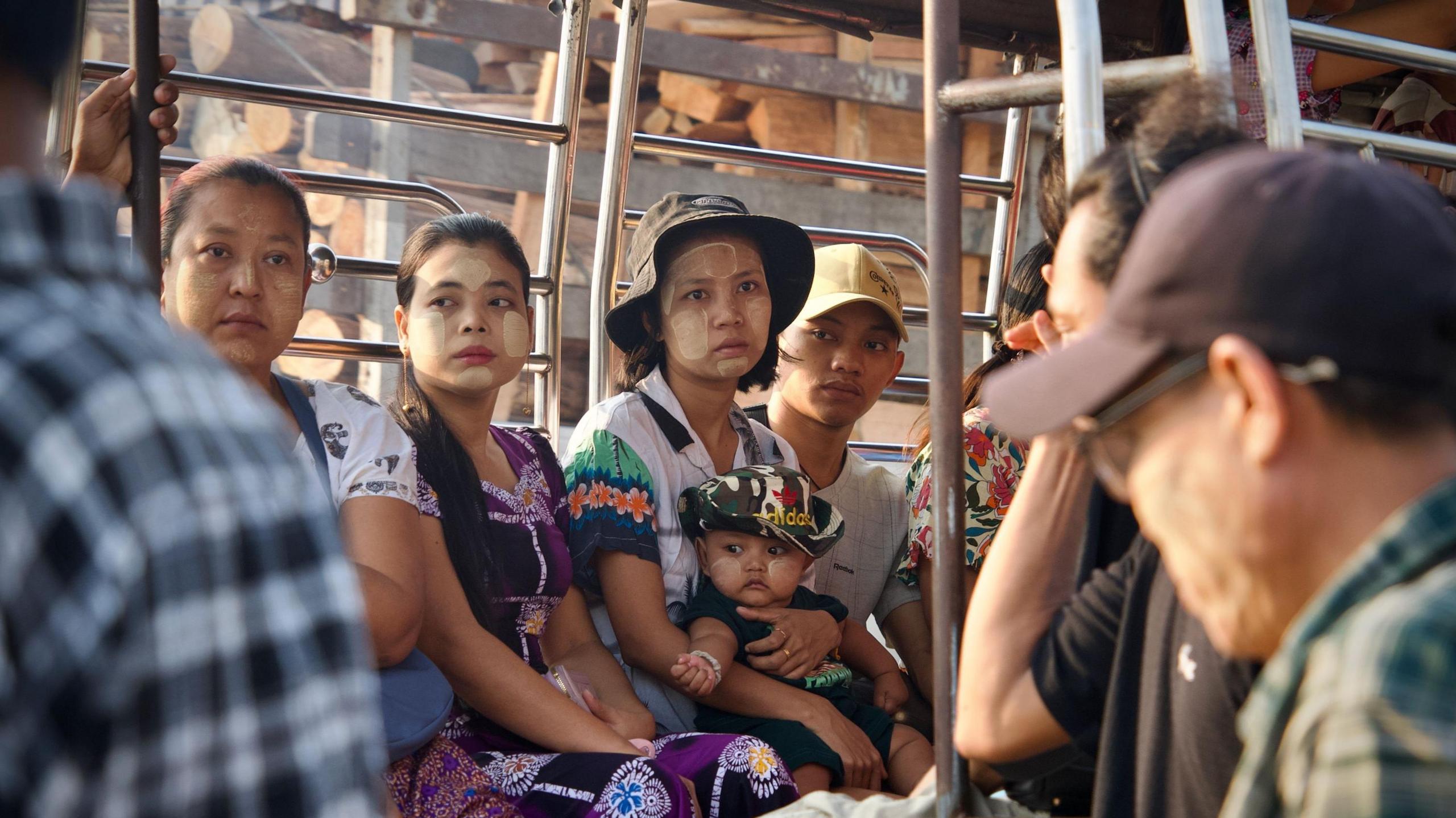 Tre gra, njëra mban një fëmijë në prehër dhe një burrë shihen në një autobus në Yangon