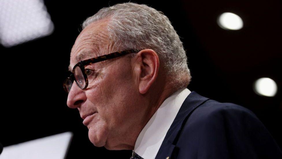 Chuck Schumer po shikon majtas dhe ka veshur një kostum të errët.