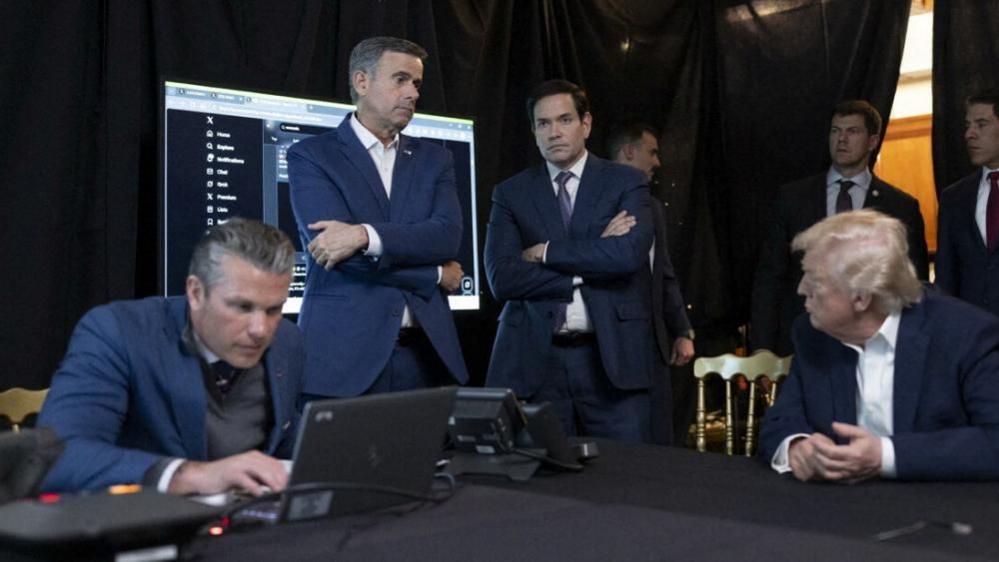 Nga e majta në të djathtë: Sekretari i Mbrojtjes Pete Hegseth, drejtori i CIA-s John Ratcliffe, Rubio dhe Trump përpara një ekrani që tregon postimet nga X.