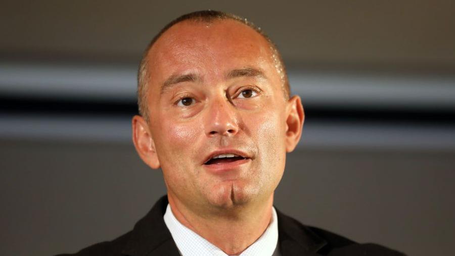 Politikani bullgar Nickolay Mladenov duke folur në mikrofon i veshur me kostum të zi dhe kravatë blu të zbehtë.