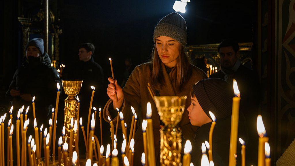 Një grua ndez një qiri me djalin e saj gjatë një shërbese nate të Krishtlindjeve në Kiev, Ukrainë, më 24 dhjetor 2025.