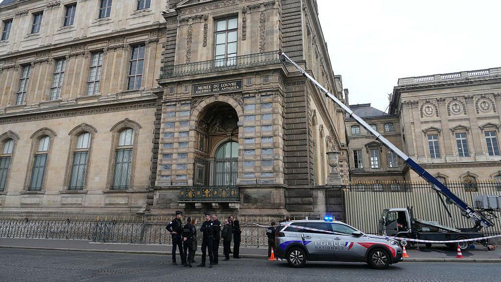 Policia qëndron në bazën e Luvrit, me shkallën mekanike që shtrihet lart drejt saj pas tyre.