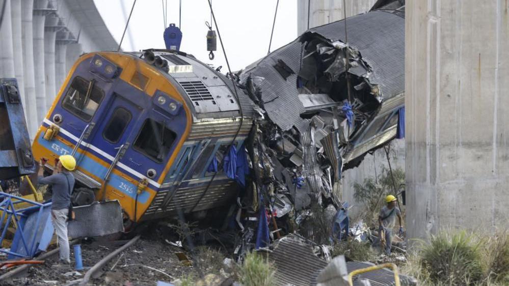 Ekipet e shpëtimit punojnë në rrënojat e një treni pasagjerësh pasi një vinç ndërtimi u rrëzua mbi të. Treni është pjesërisht i pezulluar, me pjesë të tij të shtypura plotësisht.
