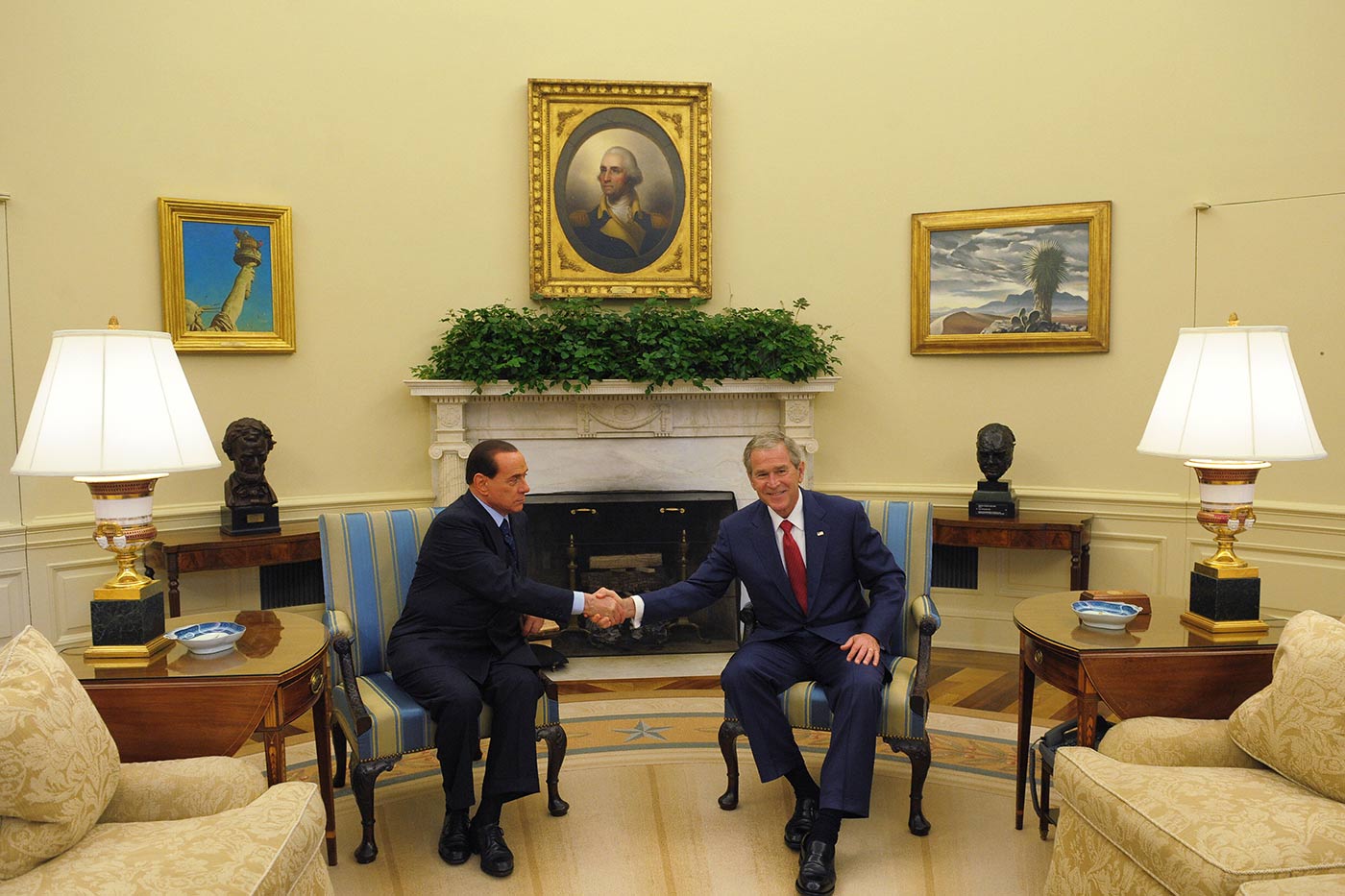 George W Bush takohet me kryeministrin italian Silvio Berlusconi, me të dy burrat të ulur në kolltuqe me vija, duke shtrënguar duart para një oxhaku të bardhë. Dhoma ka mure me ngjyrë krem ​​të butë dhe është e dekoruar me vepra arti të kornizuara, duke përfshirë një portret qendror mbi oxhak dhe dy piktura peizazhesh në të dyja anët. Një bimë e gjelbër qëndron mbi oxhak, e shoqëruar nga dy buste të errëta mbi tavolina anësore prej druri. Dy llamba të mëdha të bardha me baza ari sigurojnë ndriçim të ngrohtë.