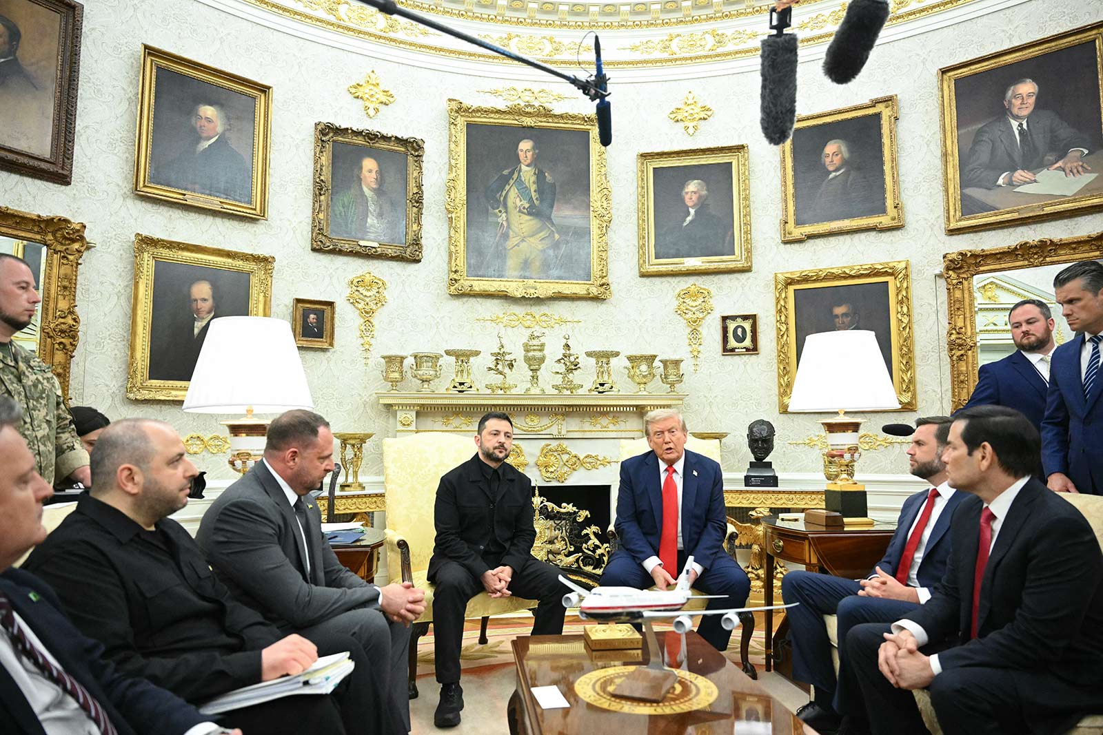 Donald Trump dhe Presidenti ukrainas Volodymyr Zelensky janë ulur në Zyrën Ovale me këshilltarët e tyre. Dhoma ka mure me ngjyrë krem ​​me detaje të zbukuruara ari dhe është zbukuruar me portrete të shumta të figurave historike të kornizave të praruara. Dy llamba të bardha rrethojnë një oxhak të zbukuruar me copa dekorative ari dhe një bust të zi. Tavani ka korniza të ndërlikuara dhe një kornizë ari.